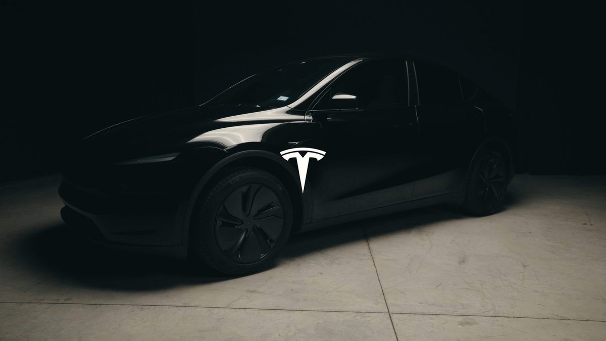 Black Tesla Model Y in a dark studio with the Tesla logo projected on its door